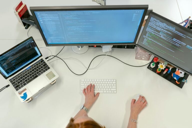 Person sitting at desk in front of laptop computer and monitors
