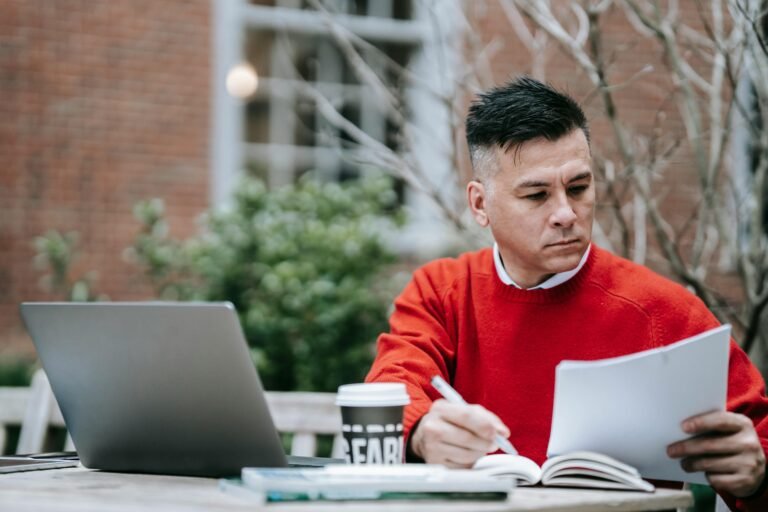 Person working at table outside with books.