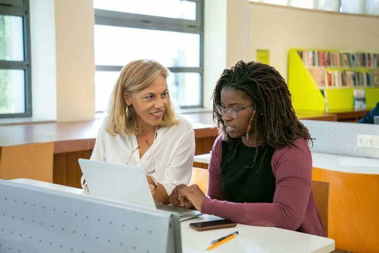 A female advisor and college student sitting at a table looking at a laptop.