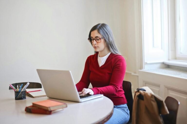 A woman sitting at a table using a laptop to write a letter.