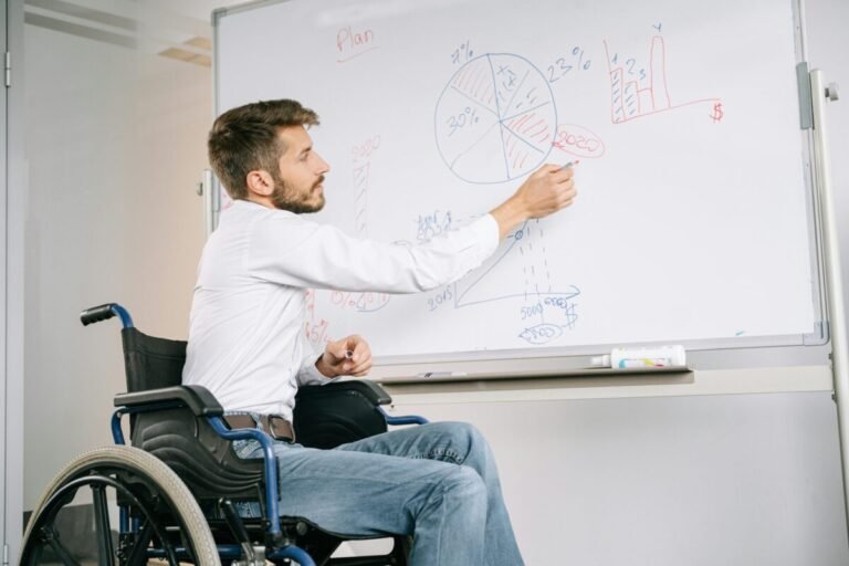 Professor in wheelchair writing on whiteboard.