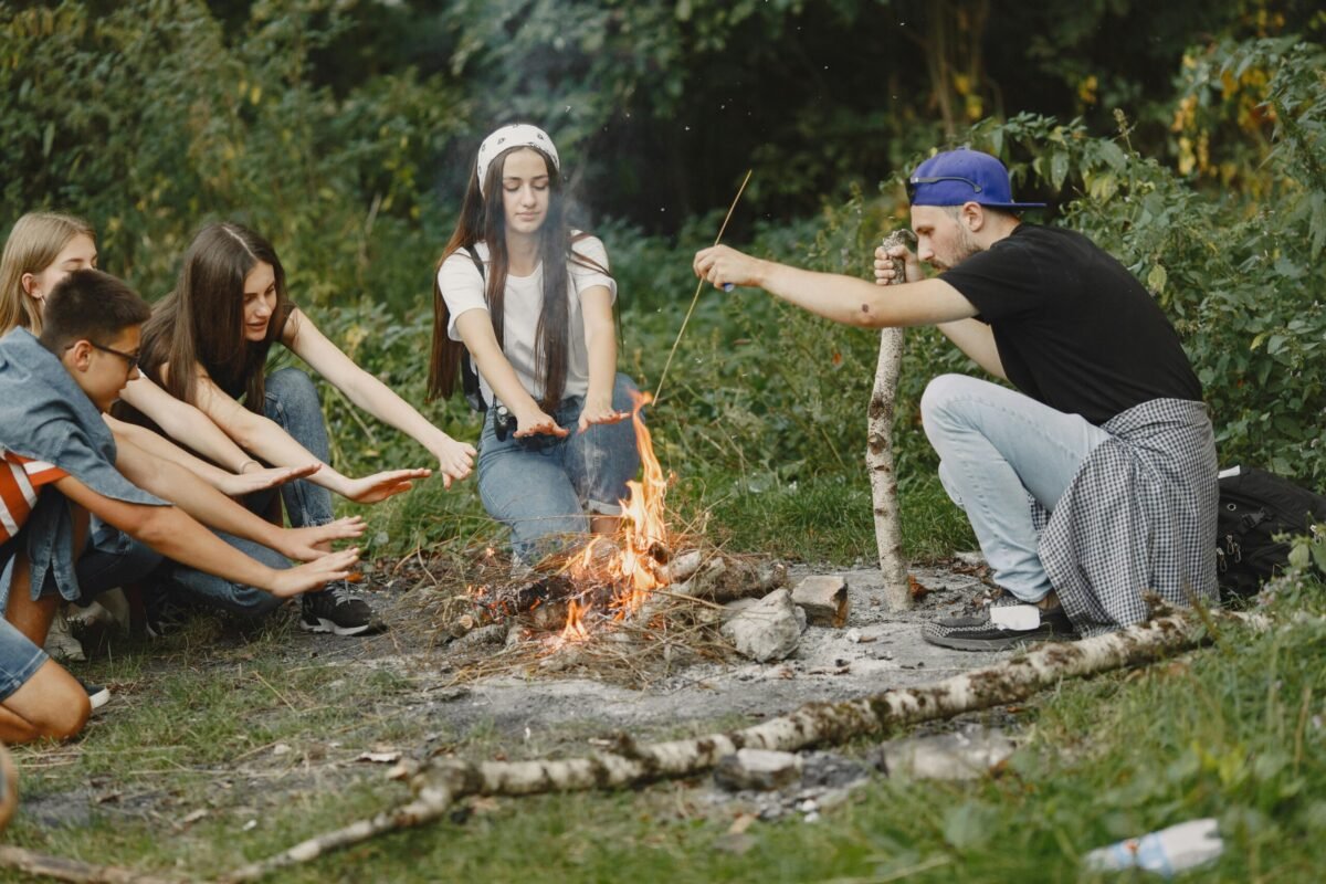 Summer camp counselor siting in front of a fire with summer campers.