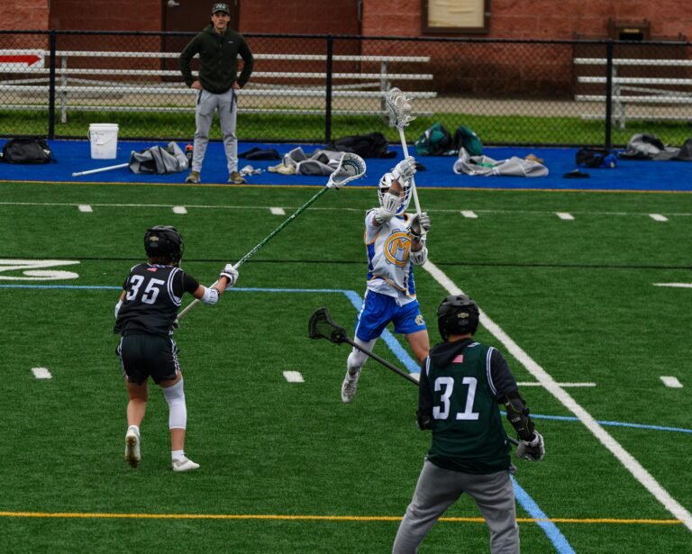 Junior varsity lacrosse coach, coaching student athletes on field.