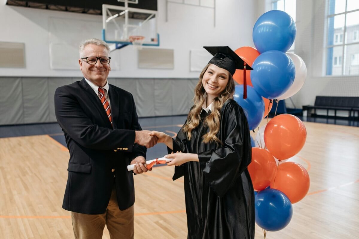 School leader and administrator shaking the hand of a student at graduation.